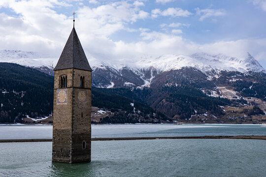 Versunkener Kirchturm im Reschensee mit schneebedeckten Bergen