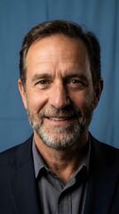 Obraz premium Professional mature Caucasian businessman with gray beard smiling confidently in dark suit against blue background for corporate headshot photography.