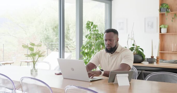 African American man in polo typing on laptop at wooden table, pausing after typing to refocus