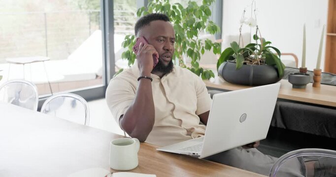 African American man in beige shirt answering call at dining table, typing on laptop working