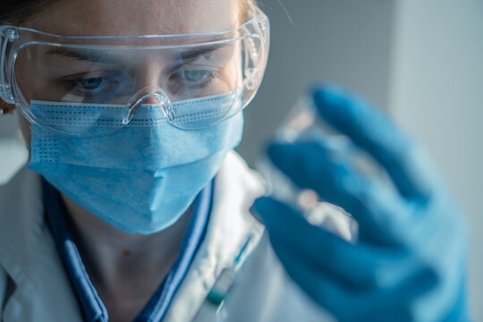 A laboratory scientist in safety gear inspects a sample vial with concentration, highlighting modern research practices. The image captures innovation and precision in scientific work