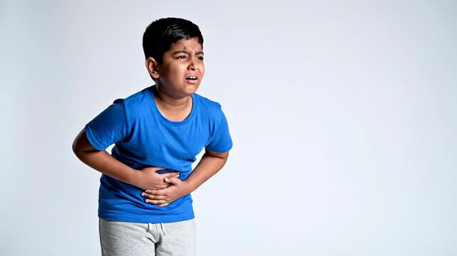sick indian child suffering from strong stomach ache. sad boy holding belly in pain against white background. food poisoning, indigestion or flu symptoms. healthcare, copyspace.