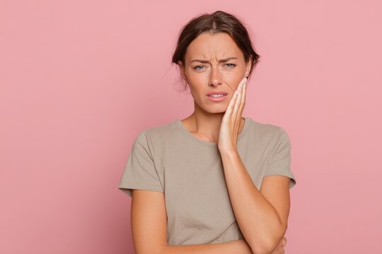 Portrait of a young woman experiencing dental pain against a pink studio backdrop