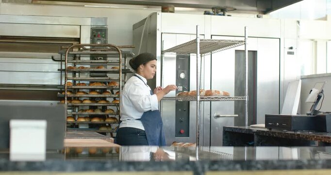 Oven dinging African-American woman aproned moving loaves in bakery placing treats in case for sale