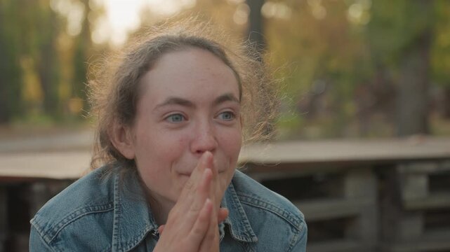 White woman in denim reacts with joyful anticipation outdoor bench at sunset hands clasped near mouth playful grin tearful eyes warm autumn light candid portrait capturing intimate marriage and family
