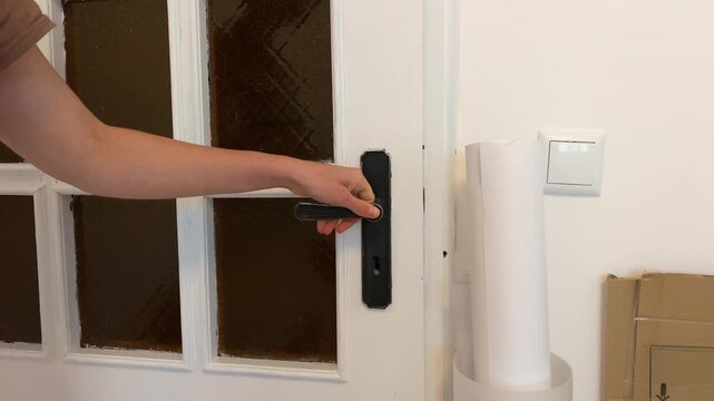 Close-up video of a person's hand grabbing a doorknob and then turning a key in the lock. The scene shows the action of locking or unlocking a white front door in a home or apartment.
