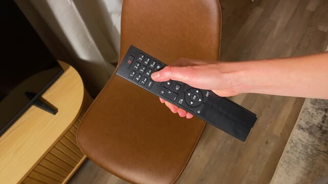 Close-up video of a hand holding a black remote control and pressing the number 8 button. Person changing channels or inputting a number on a TV or other device. POV shot.