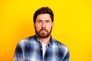 Obraz premium Surprised man with glasses and beard in plaid shirt against bright yellow background showing anxious, shocked facial expression in studio portrait