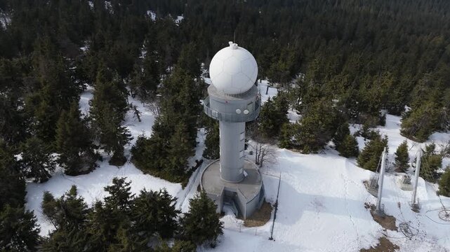 Aerial view of a weather radar station and communication towers on a snowy mountain peak at spring