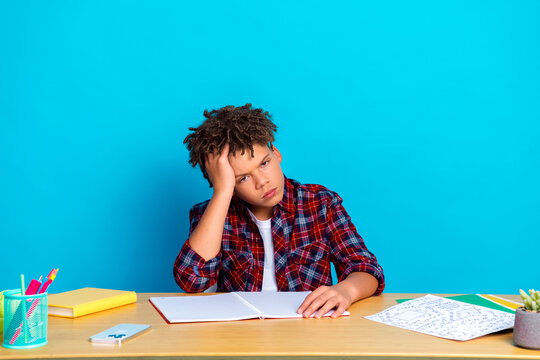 Tired teenage student frustrated with homework at desk looking bored and stressed while studying against a bright blue background
