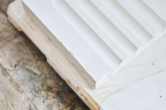 Close up of white moulded plaster decorative trim with stepped profile on wooden surface for interior design and construction detail. Manufacture and construction of moulds 