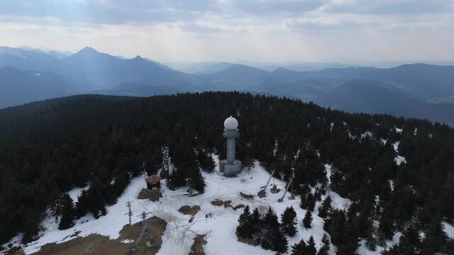 Aerial view of a weather radar station and communication towers on a snowy mountain peak at spring