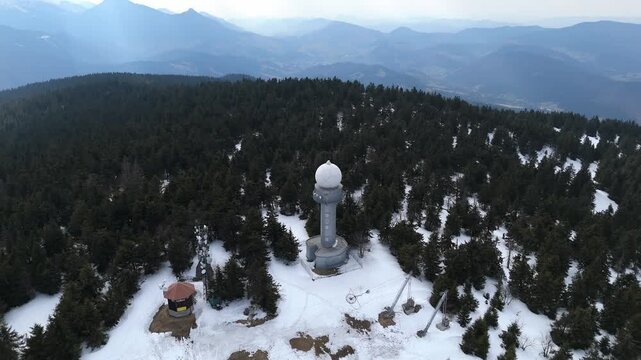 Aerial view of a weather radar station and communication towers on a snowy mountain peak at spring