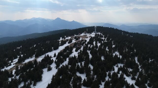 Aerial view of a weather radar station and communication towers on a snowy mountain peak at spring