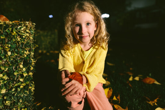 Smiling little girl holding autumn leaf at night in dramatic light outdoors
