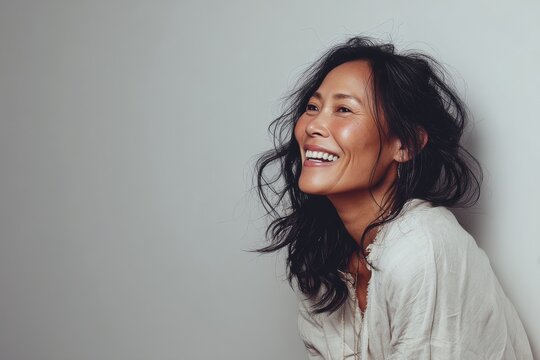 Portrait of a jovial asian woman in her 40s smiling at the camera in plain cyclorama studio wall