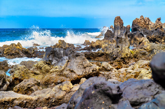 Massive surf crashes into rugged lava coastline on Lanzarote beneath deep blue summer sky. Powerful ocean surf at black volcanic rocks