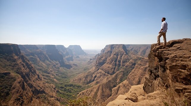 Man Standing on Cliff Edge Overlooking Deep Canyon Landscape