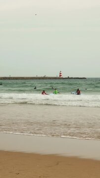 Surfing lesson on a sandy beach with a red and white lighthouse in the background.