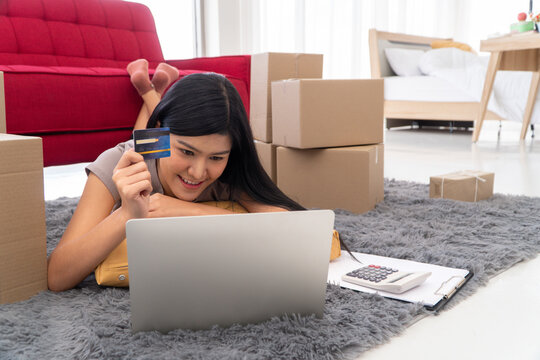 Digital Dreams: A woman lounges comfortably at home, captivated by the world of online shopping, credit card in hand. Exploring digital realms through her laptop.