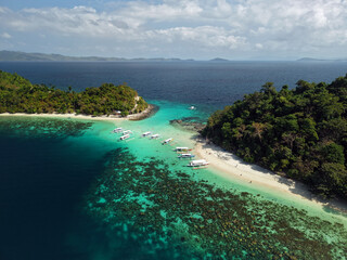 Fototapeta premium Aerial drone view of Twin Reef in Port Barton, Palawan, Philippines, featuring crystal clear turquoise waters, vibrant coral reefs, and traditional Filipino outrigger boats (bangkas).