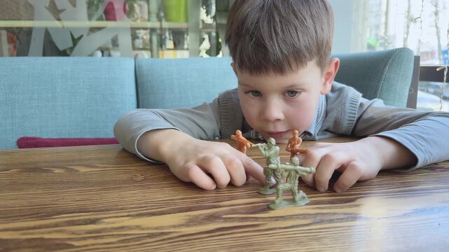  Boy creates battle scenario with toy soldiers on table. Concept of imagination, storytelling and childhood play. Useful for education, creativity and parenting content.