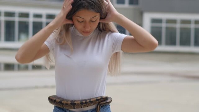 Young woman holding python snake around her waist in abandoned urban environment, wild animal concept