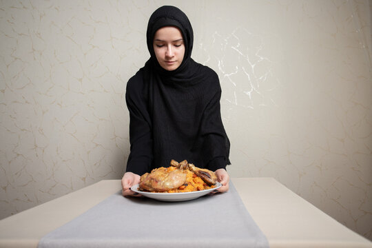 young woman in hijab presents a large plate of chicken kabsa over a neat table runner, suited to themes of ramadan dinner, gulf hospitality, halal food and festive home cooking