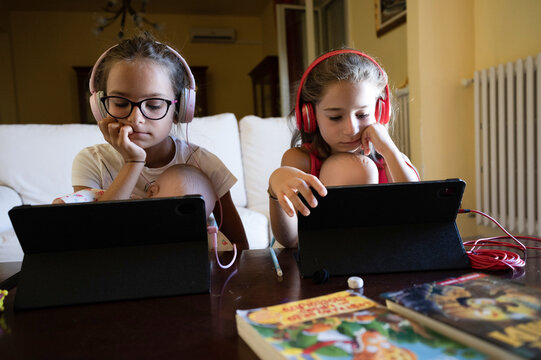 Ragazze di 11 anni sedute davanti ad un tablet con le cuffie alle orecchie.
