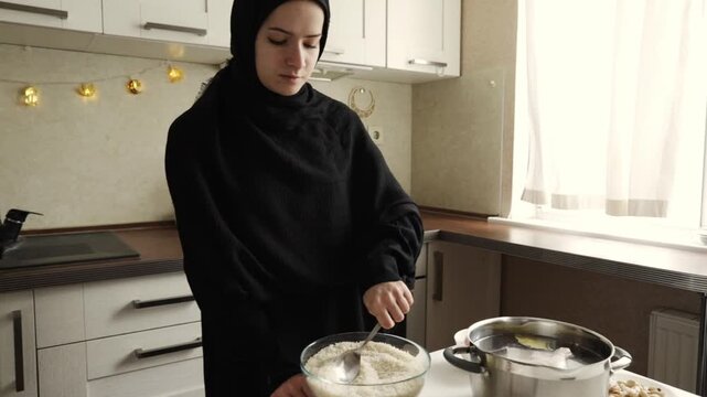muslim woman in black hijab stirring cooked rice in a large glass bowl beside pot on the table during home meal preparation for iftar or eid