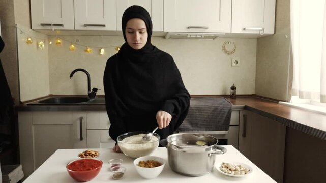 muslim woman in black hijab stirring rice in a glass bowl near cooking pot and ingredients during home iftar meal preparation for ramadan