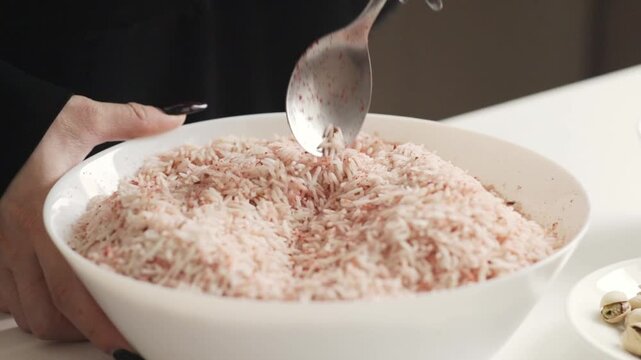 a spoon lifting long grain basmati rice lightly tinted with red seasoning, highlighting texture and spice distribution during preparation of a savory rice dish