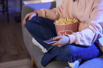 Woman with tasty popcorn watching movie on sofa at home late in evening