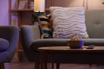 Tasty popcorn with TV remote controller on table in living room at night