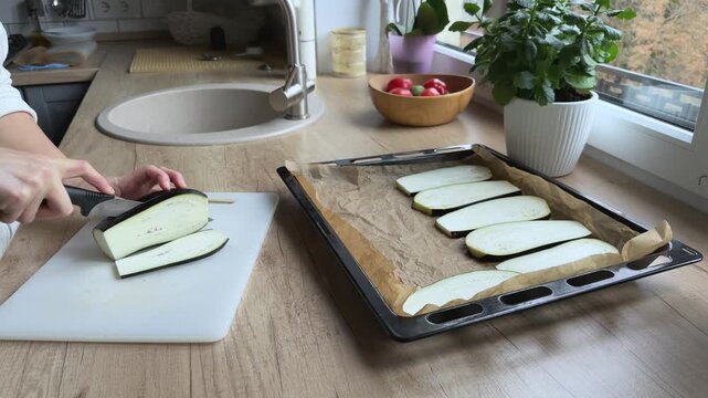 Cutting eggplant into thin slices on board Preparing fresh vegetables for baking dish
