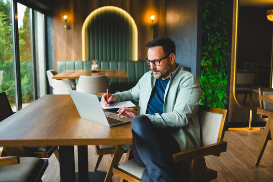 Man working on laptop and taking notes in modern caf