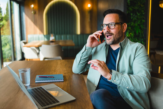 Businessman having phone call while working on laptop in cafe