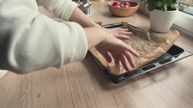 Hands crumpling parchment paper and placing it on tray Preparing surface for baking vegetables in oven 