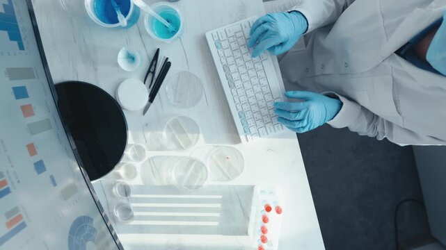 Top view of laboratory scientist conducting experiments with petri dishes, pipette, and computer keyboard. Innovative research, biotechnology, and data driven science in a high tech lab setting
