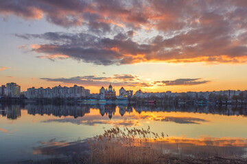 Golden sunset melts over Obolon embankment in Kyiv, painting the Dnipro River with shimmering reflections. Clouds drift softly as glowing domes and skyline dissolve into a calm, dreamy evening. © elena_suvorova