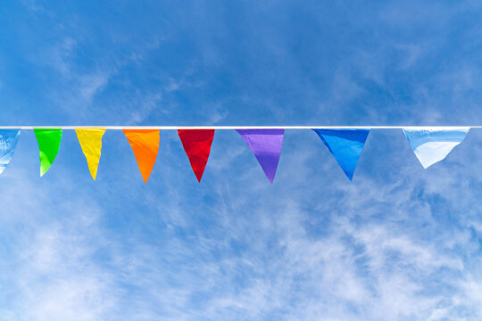 Colorful triangular pennant flags hanging on a line, in a bright photographic style, set against wispy clouds sky, symbolizing celebration