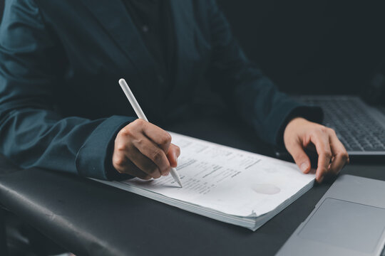 Blurred close-up of hand signing business contract on desk with laptop in background, representing legal documentation, agreement process, corporate deals, and professional office workflow.