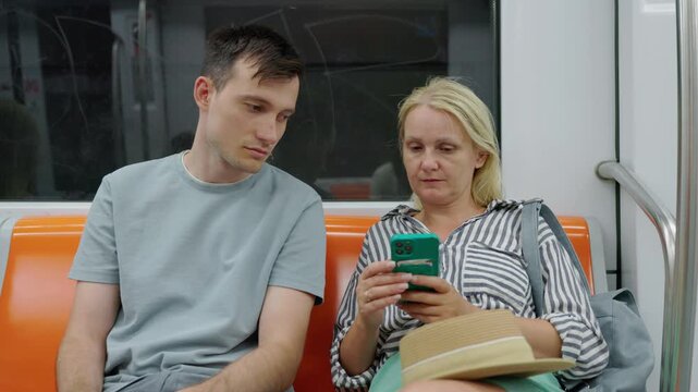 Man and woman sitting in subway train discussing smartphone content, urban commute and communication concept