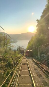 Funicular ascending through tunnel to Brunate overlooking Lake Como at sunset, scenic railway journey with dramatic exit revealing city skyline, mountains and glowing Italian landscape