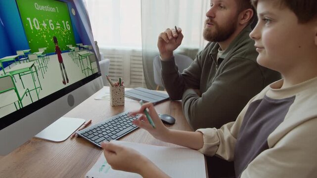 Side view of Caucasian gen Alpha boy doing Math exercise in computer game with father sitting at table while learning together at home