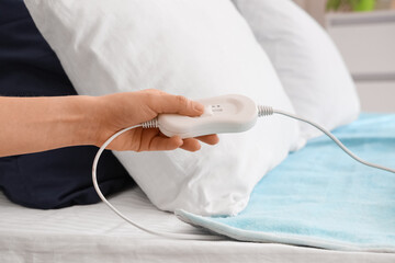 Female hand turning on electric heating pad in bedroom, closeup © Pixel-Shot