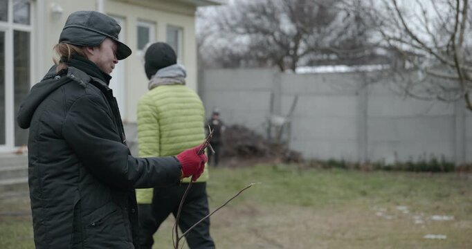 Men with kid cut branches in backyard and stockpile firewood in shed for winter. 4K 10-bit