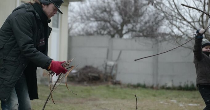 Men with kid cut branches in backyard and stockpile firewood in shed for winter. 4K 10-bit
