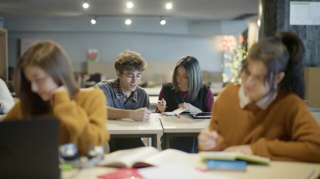 Young students are focused on their studies, collaborating and working individually at desks. Diverse university students engage in active learning and discussion in a modern classroom.