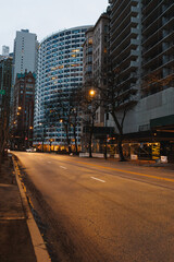Fototapeta premium City street during early evening with tall buildings and street lights in a urban setting